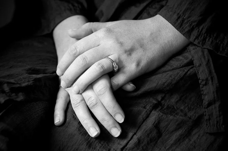Black and white photo of a person with hands resting on lap, wearing a ring on one finger.