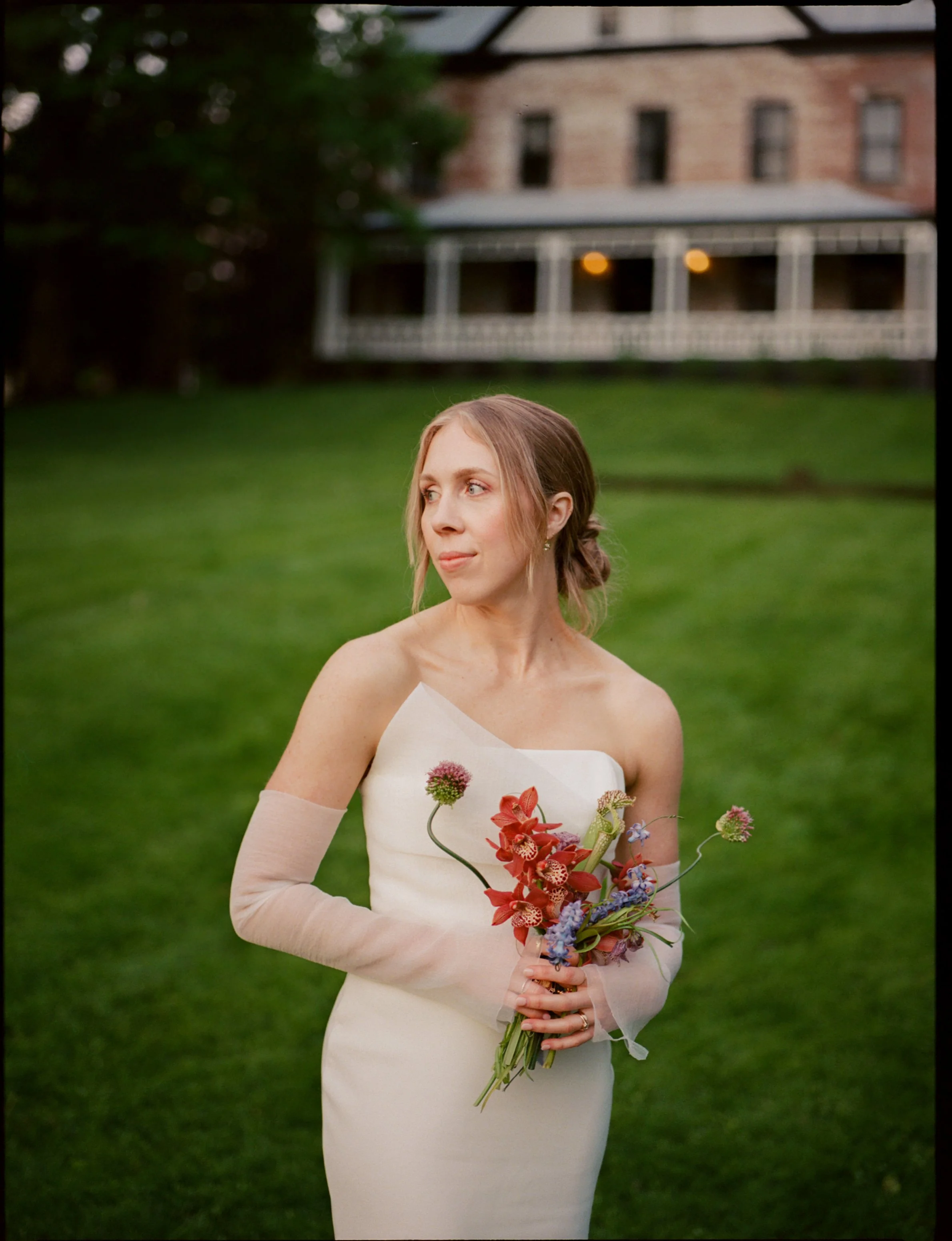 Sydney holds whimsical petite bouquet in front of Elizabeth House in Leeds, NY at her intimate backyard micro-wedding in the Catskills. Film photography by Mikala Gallo Photography.