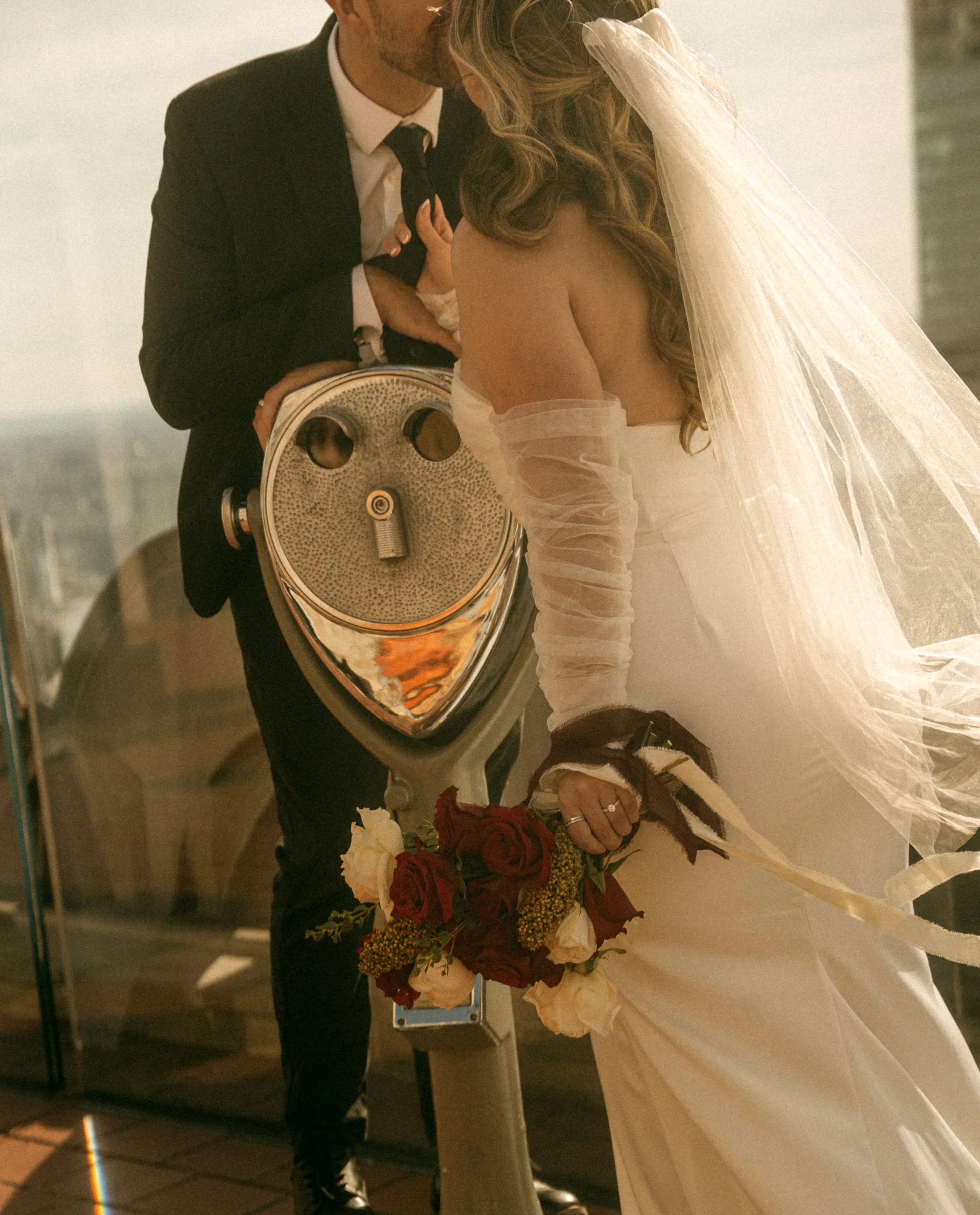 Tim & Emily whisper sweet nothings at "Top of The Rock."  Emily holds a gorgeous red and white classic bouquet designed by Catskills based florist, Raving Flamingo Flowers. Photo by Brittany Dobrowski, makeup by Lemony NYC.