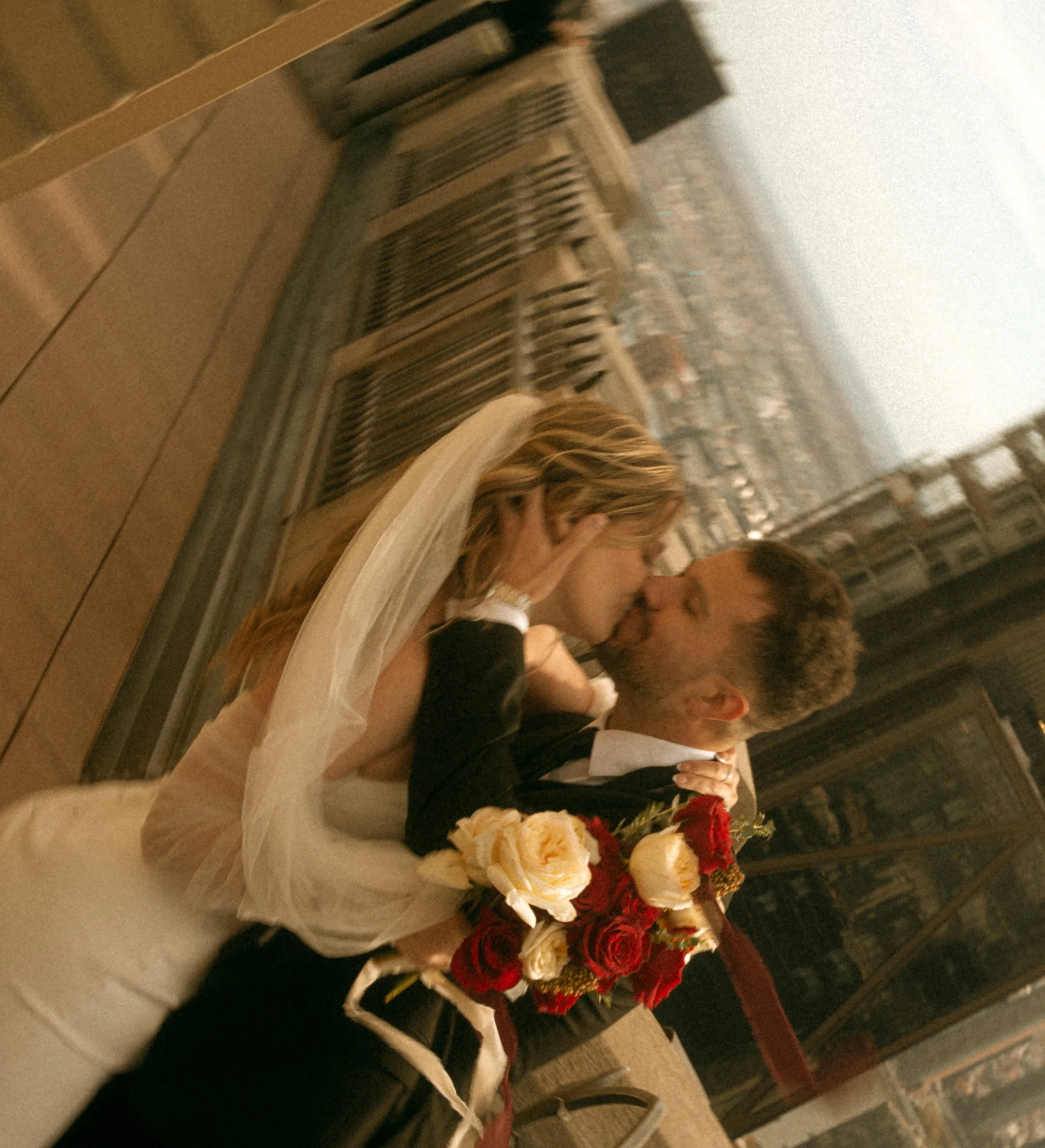 Tim & Emily kiss at "Top of The Rock."  Emily holds a gorgeous red and white classic bouquet designed by Peekskill based florist, Raving Flamingo Flowers. Photo by Brittany Dobrowski, makeup by Lemony NYC.