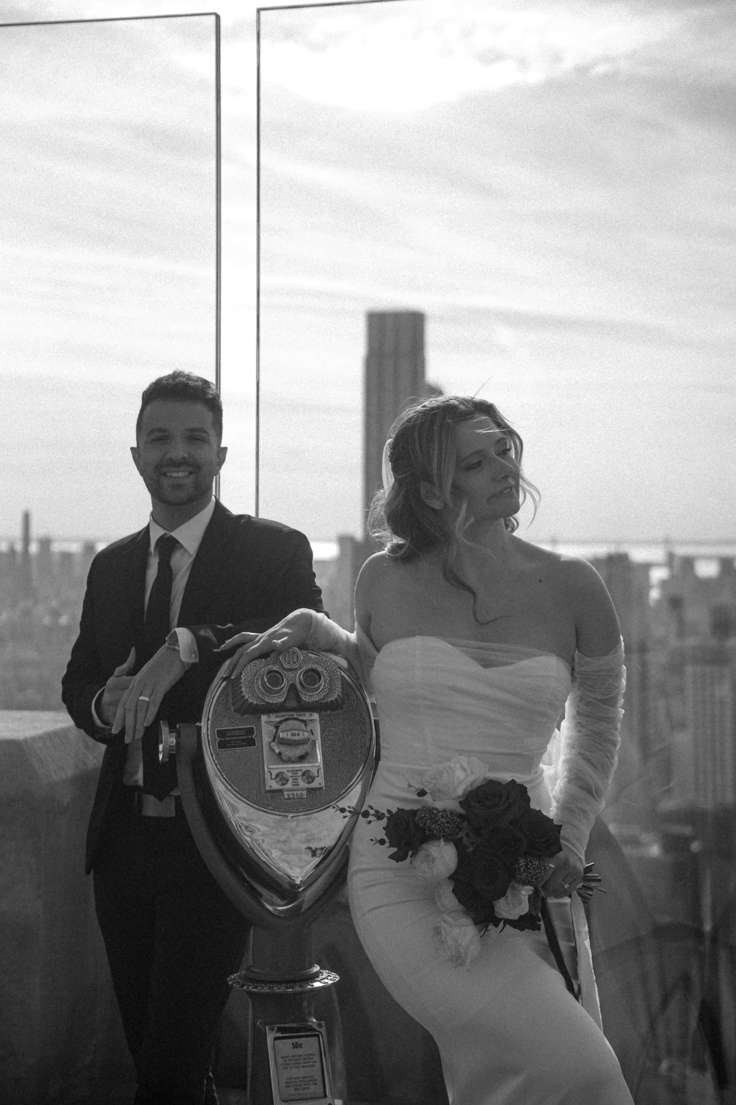 Tim & Emily at "Top of The Rock" at Rockefeller Center in NYC.   Emily holds a gorgeous red and white classic bouquet designed by New York City and Brooklyn florist, Raving Flamingo Flowers. Photo by Brittany Dobrowski, makeup by Lemony NYC.