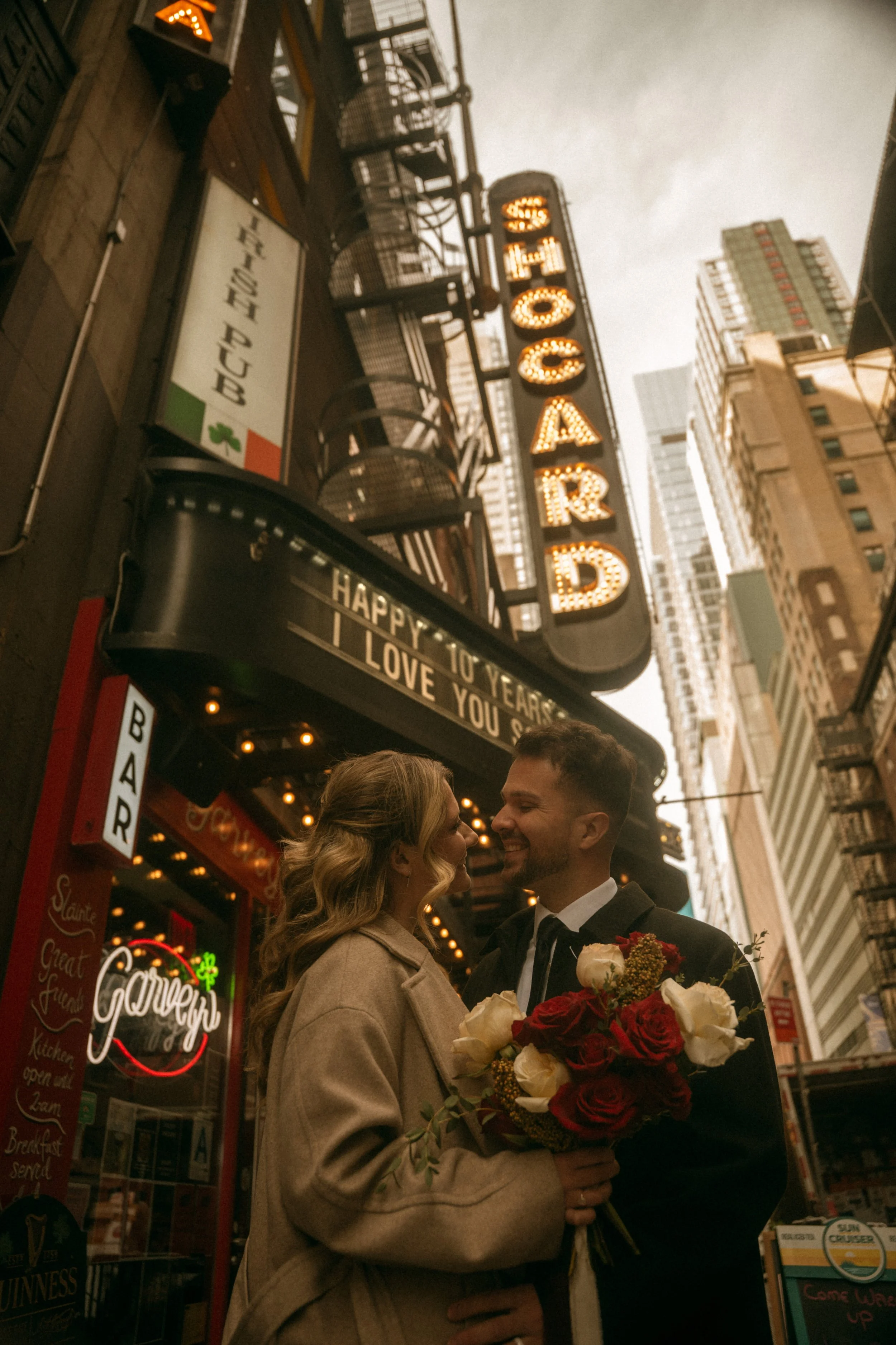 Tim & Emily kiss in front of the Shocard sign, celebrating their 10th anniversary.  Emily holds a gorgeous red and white classic bouquet designed by Hudson Valley based florist, Raving Flamingo Flowers. Photo by Brittany Dobrowski, makeup by Lemony N