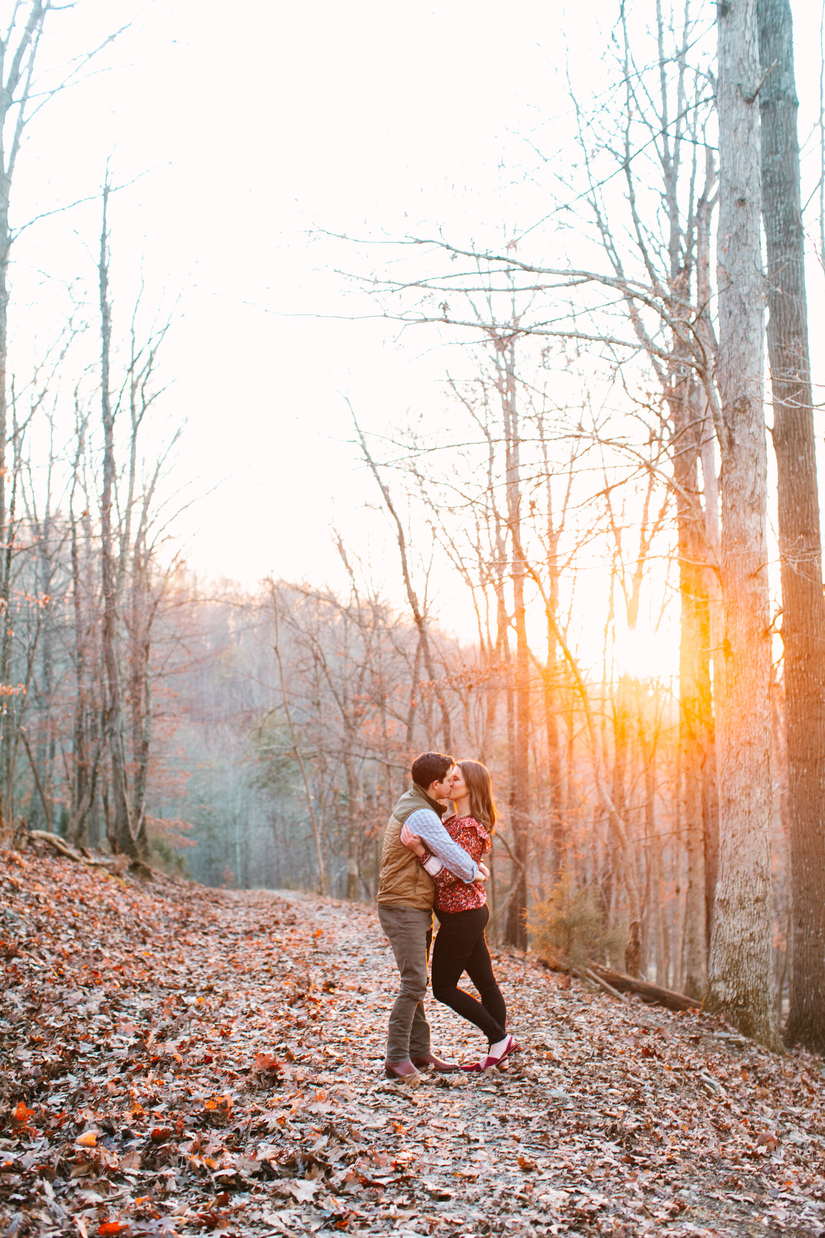 Couple Kissing at Sunset In The Woods During Family Farm Winter Engagement Photo Session