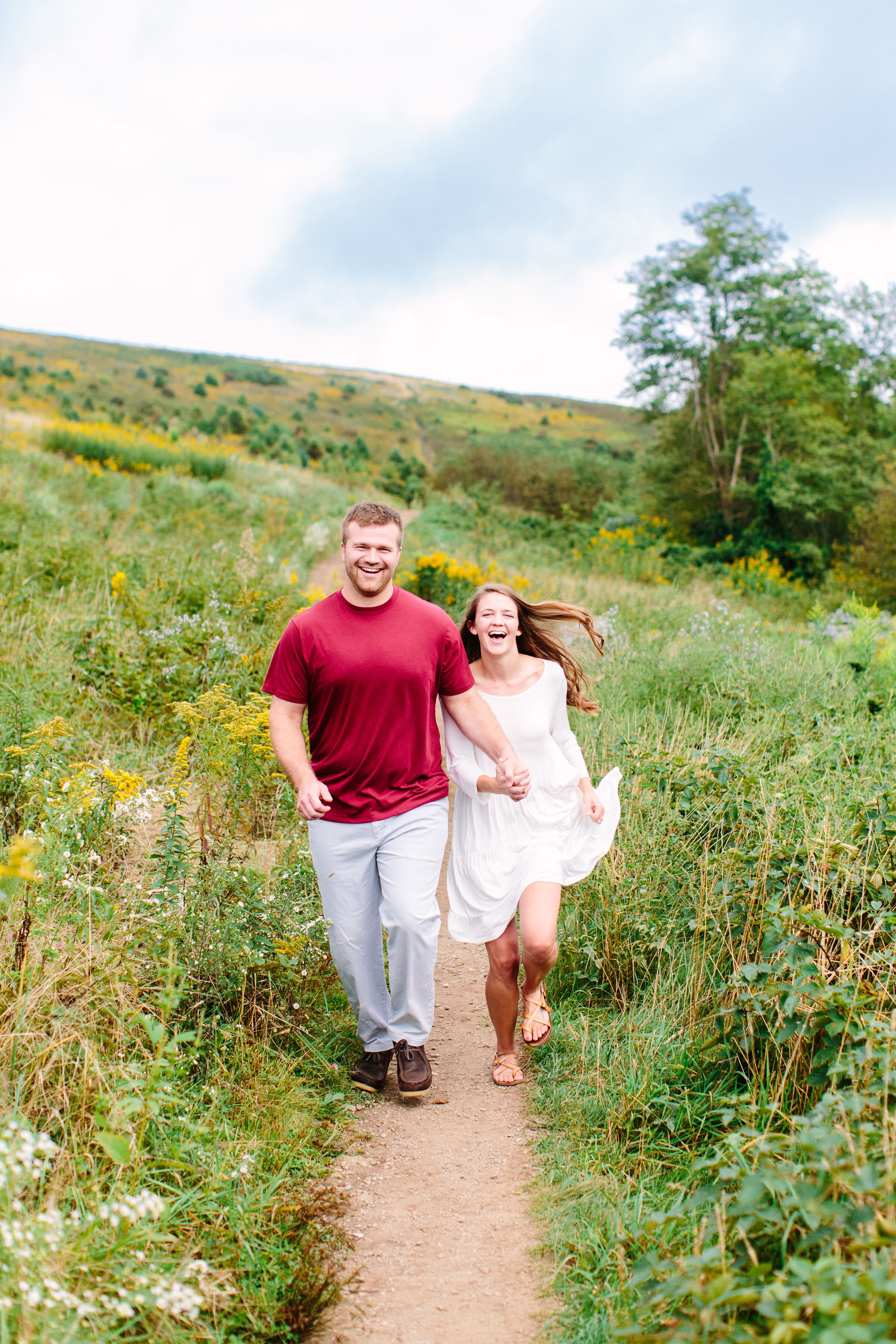 Max Patch Summer Engagement Photos on the Flower-covered Mountaintop | Couple running hand in hand