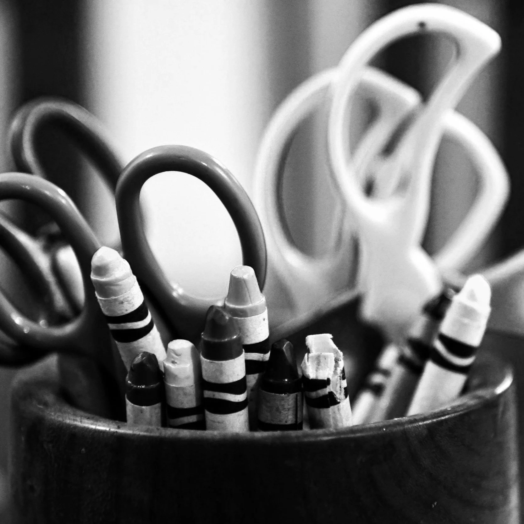 Black and white close-up of striped crayons and looped paper clips in a container.