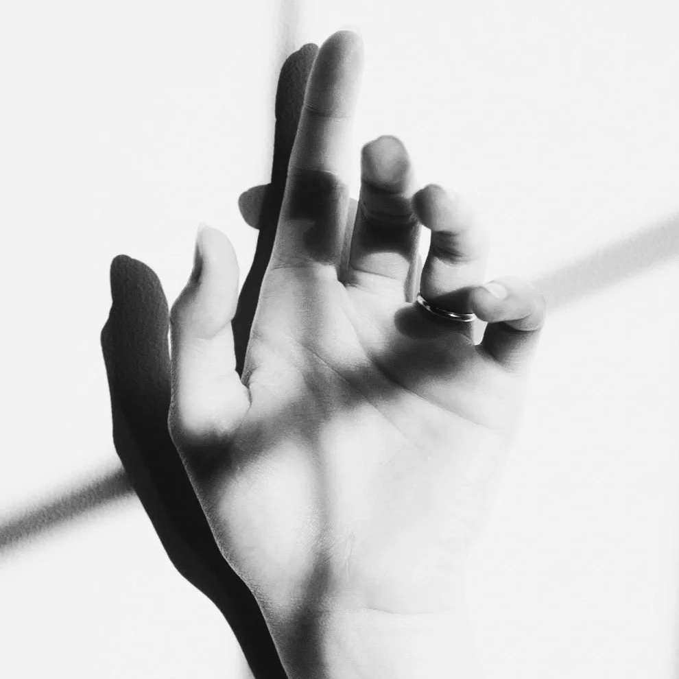 A black and white photo of a human hand with fingers partially bent, casting a shadow on a white background.