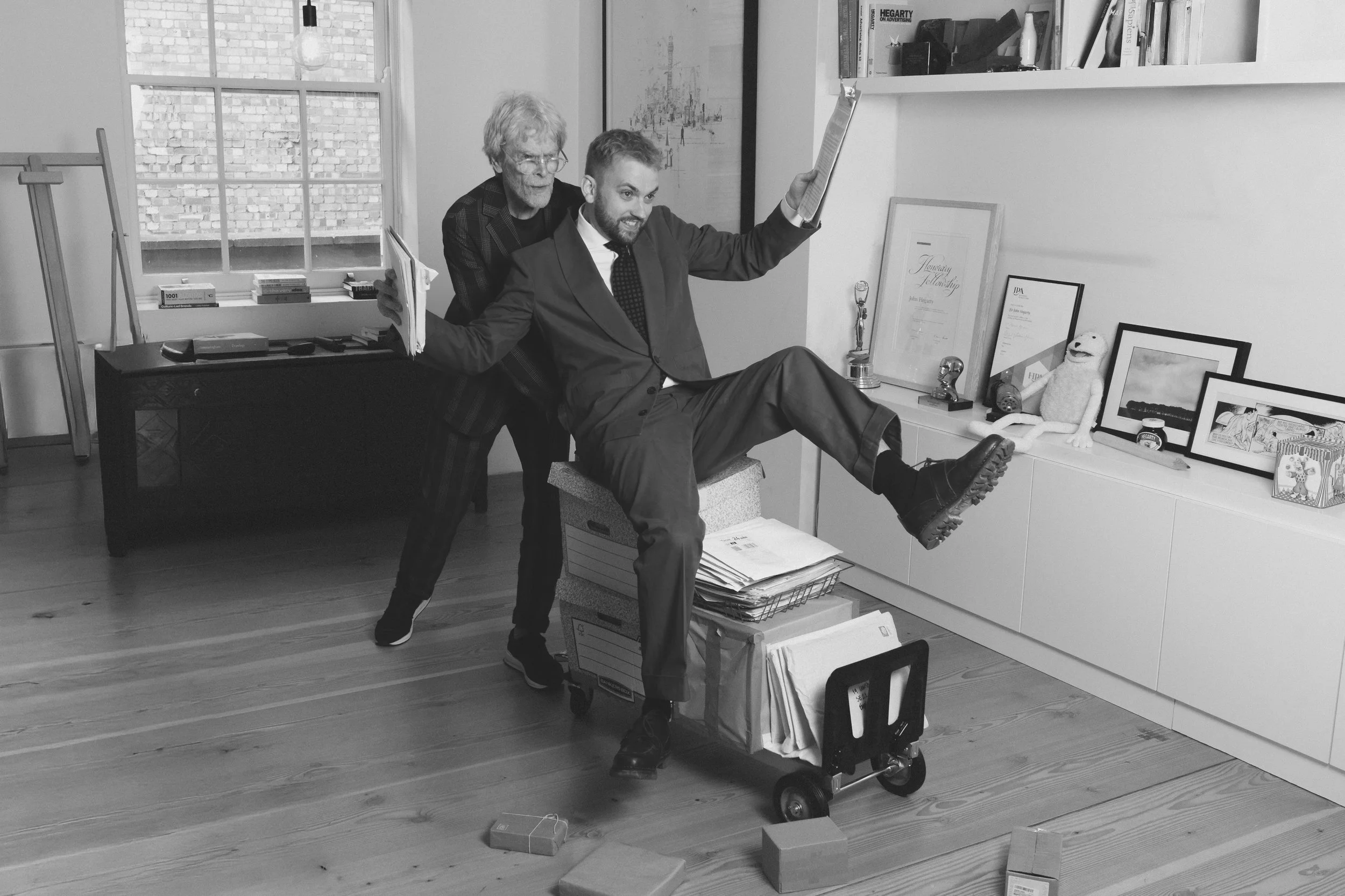 John Hegarty pushes RVBBERDUCK on a mail trolley in an office.