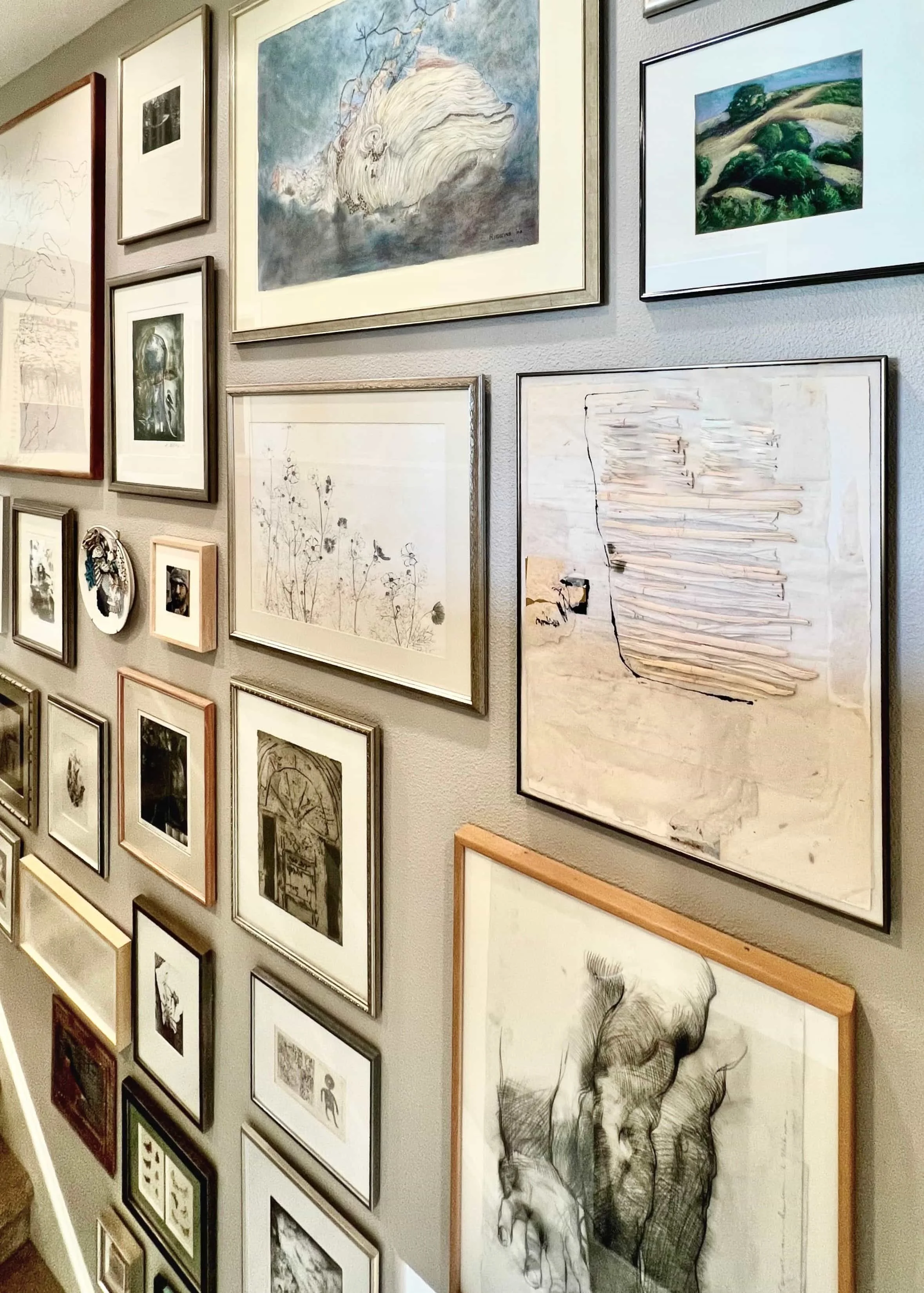 Gallery wall with various framed artworks including abstract, botanical, and landscape drawings and paintings.
