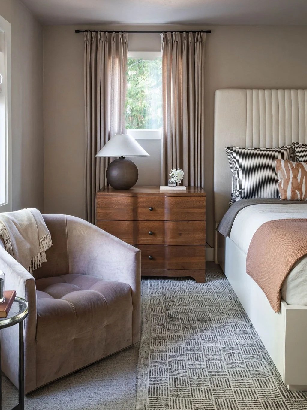 Layered bedroom with swivel chair, wallpaper, drapes, upholstered bed.