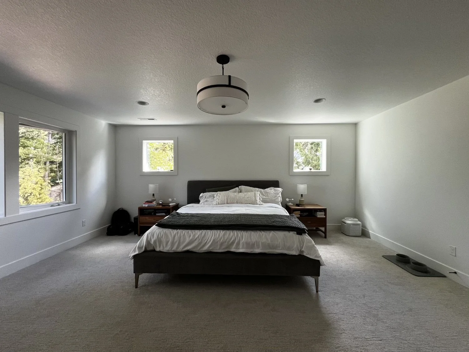 Primary bedroom with a centered upholstered bed, matching nightstands, soft gray walls, plush carpet, and modern ceiling light, creating a calm and minimal retreat.