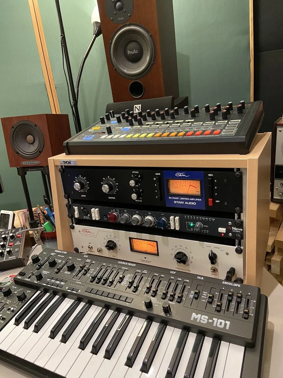 Music studio equipment including a keyboard, source mixer, amplifiers, and speakers in a recording studio.