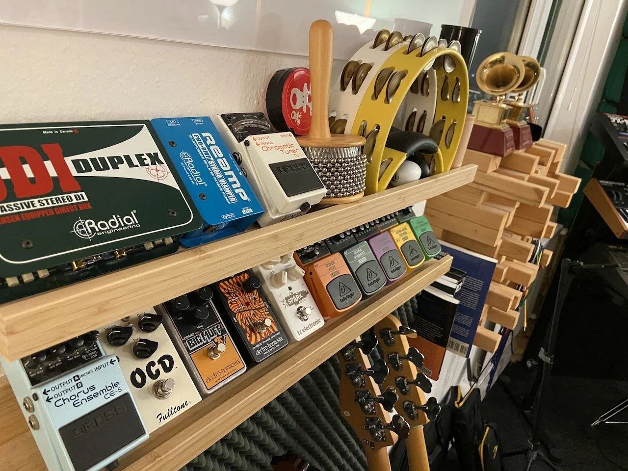 Collection of musical equipment and accessories including guitar pedals, tambourines, and a headstock of a guitar in a studio or music room.