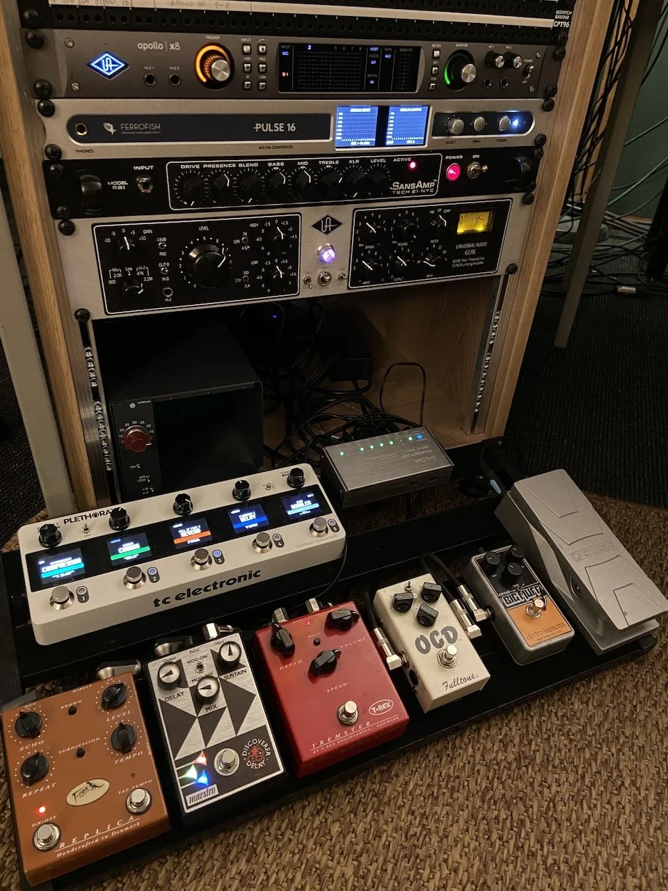 A rack with audio equipment and various guitar pedals on a pedalboard.