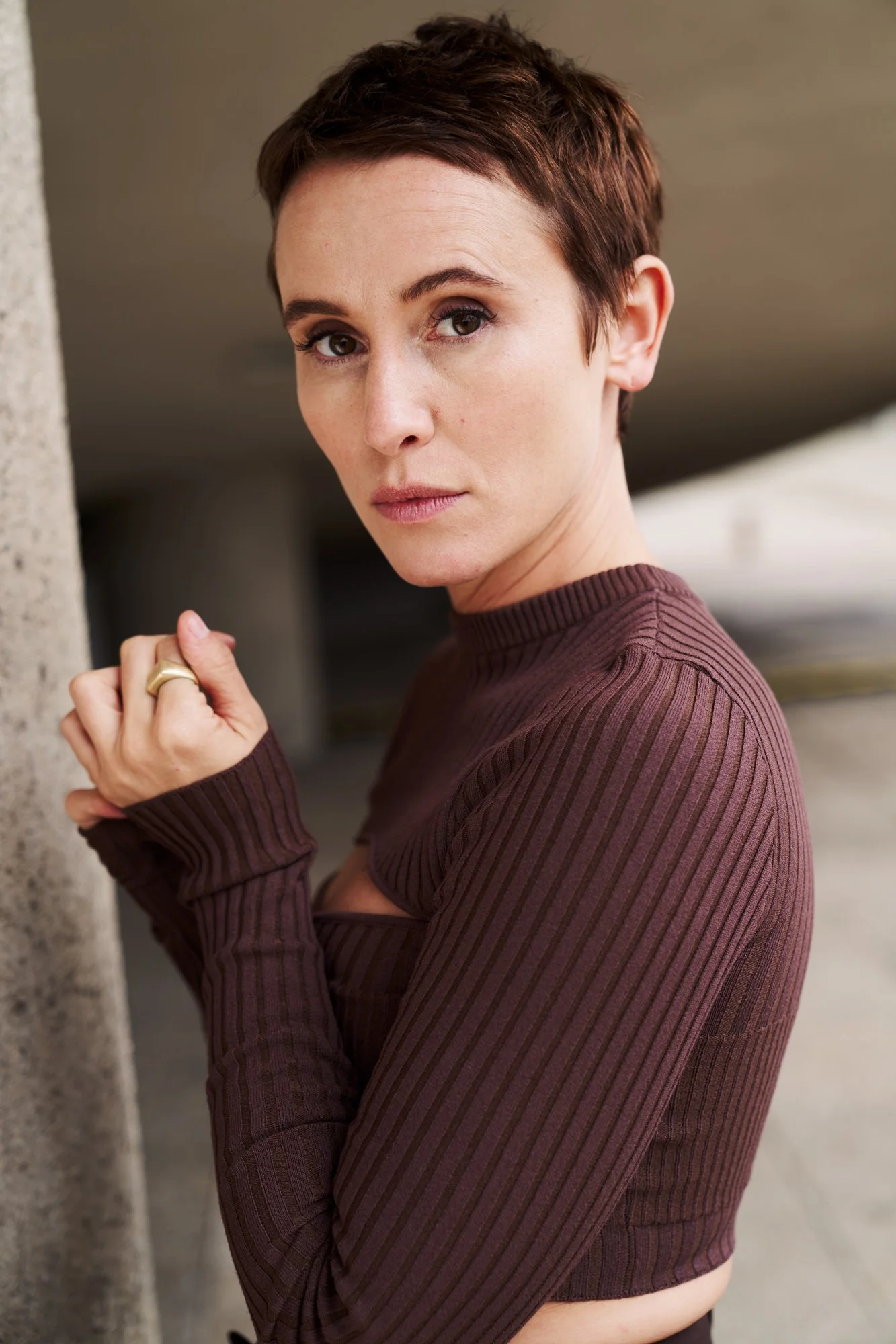 Porträtaufnahme der Schauspielerin Peri in braunem Rippstrickoberteil mit goldenem Ring, an eine Betonsäule gelehnt, seitlicher Blick in die Kamera, fotografiert von Koszki Photography Berlin.

Peri Baumeister war 2012 im “Tatort: Borowski und der st