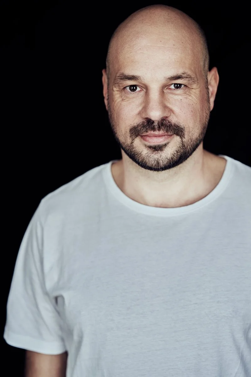 Farbporträt des DJs D-Nox im weißen T-Shirt vor schwarzem Hintergrund mit ruhigem, direktem Blick, fotografiert von Koszki Photography Berlin.