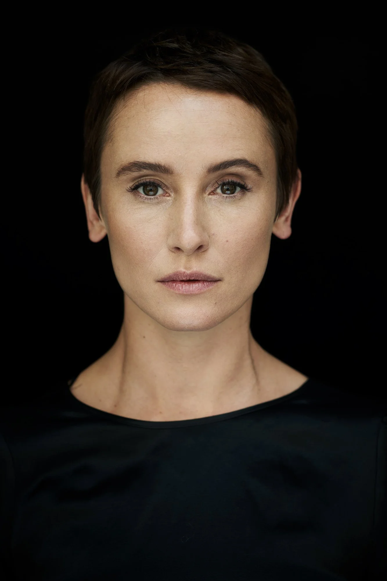 Headshot der Schauspielerin Peri Baumeister im schwarzen Top vor schwarzem Hintergrund, frontaler Blick in die Kamera, fotografiert von Koszki Photography Berlin.