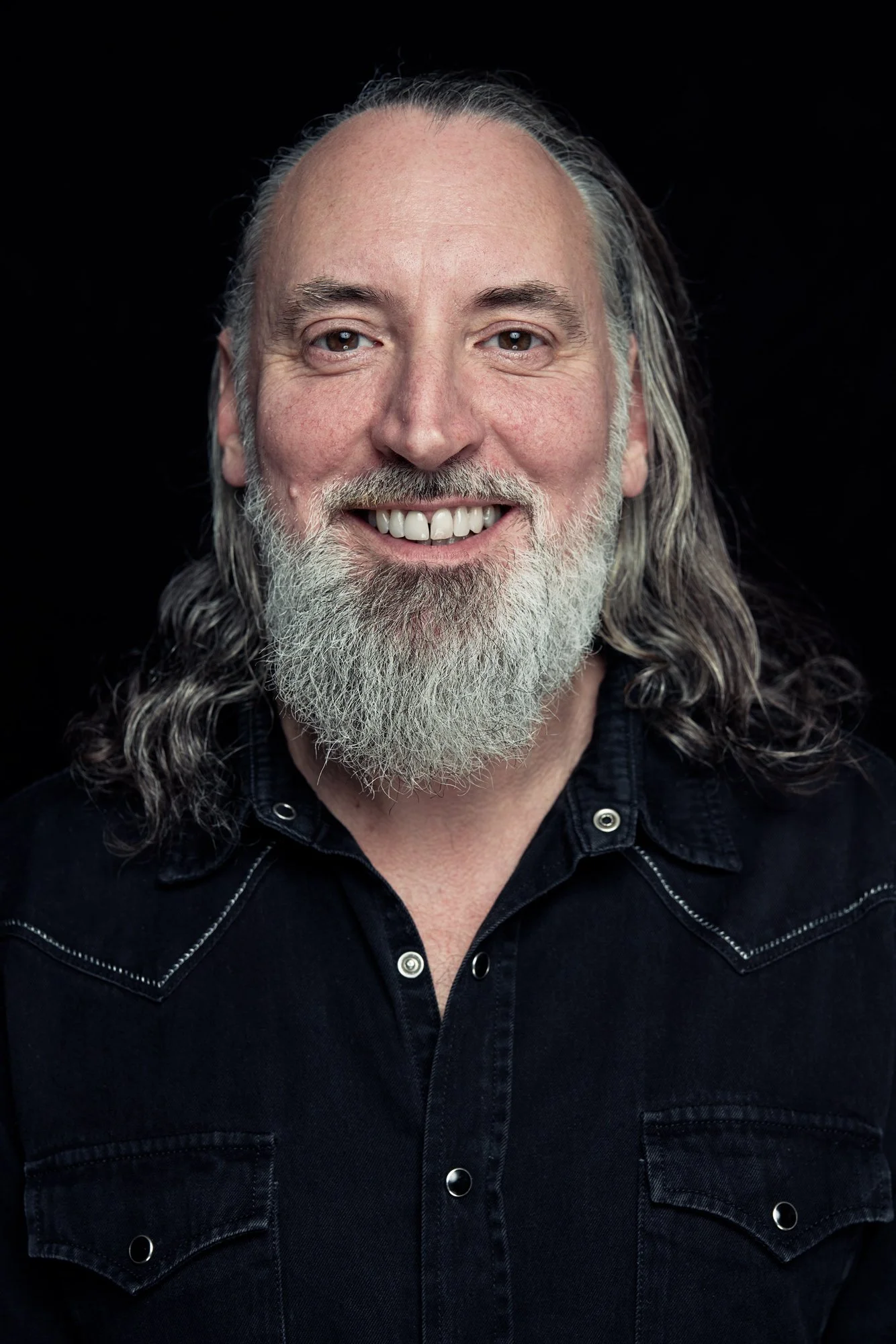 Musiker Fink als herzlicher Headshot vor schwarzem Hintergrund, Vollbart, langes Haar, offenes Lachen. Fotografiert von Koszki Photography Berlin.