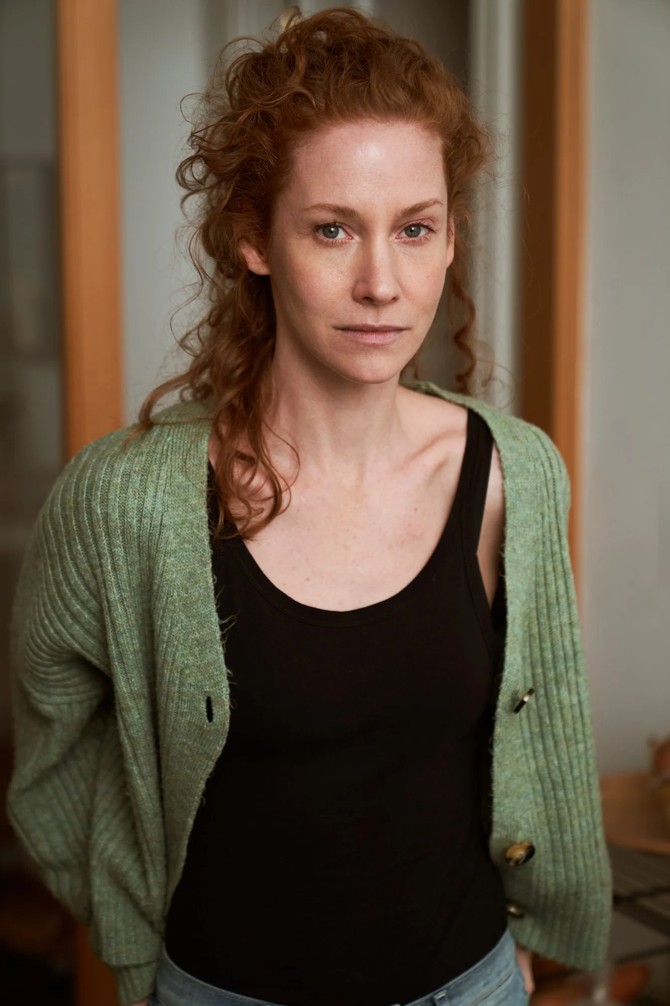 Porträtaufnahme der Schauspielerin Sina-Valeska Jung mit lockigem rotem Haar in grüner Strickjacke und schwarzem Top, ruhiger Blick in die Kamera, fotografiert von Koszki Photography Berlin.