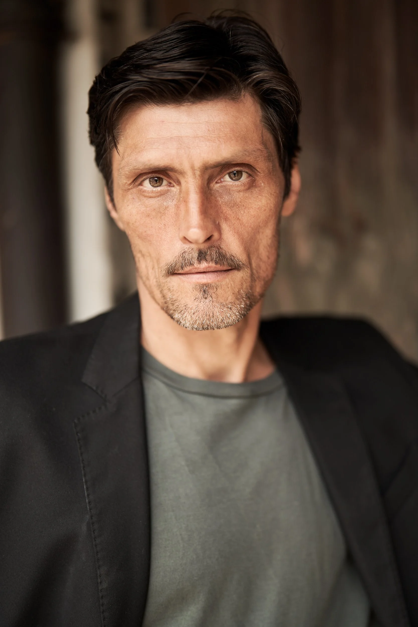 Headshot des Schauspielers Stipe Erceg im dunklen Sakko und graugrünen T-Shirt mit direktem Blick, fotografiert von Koszki Photography Berlin.