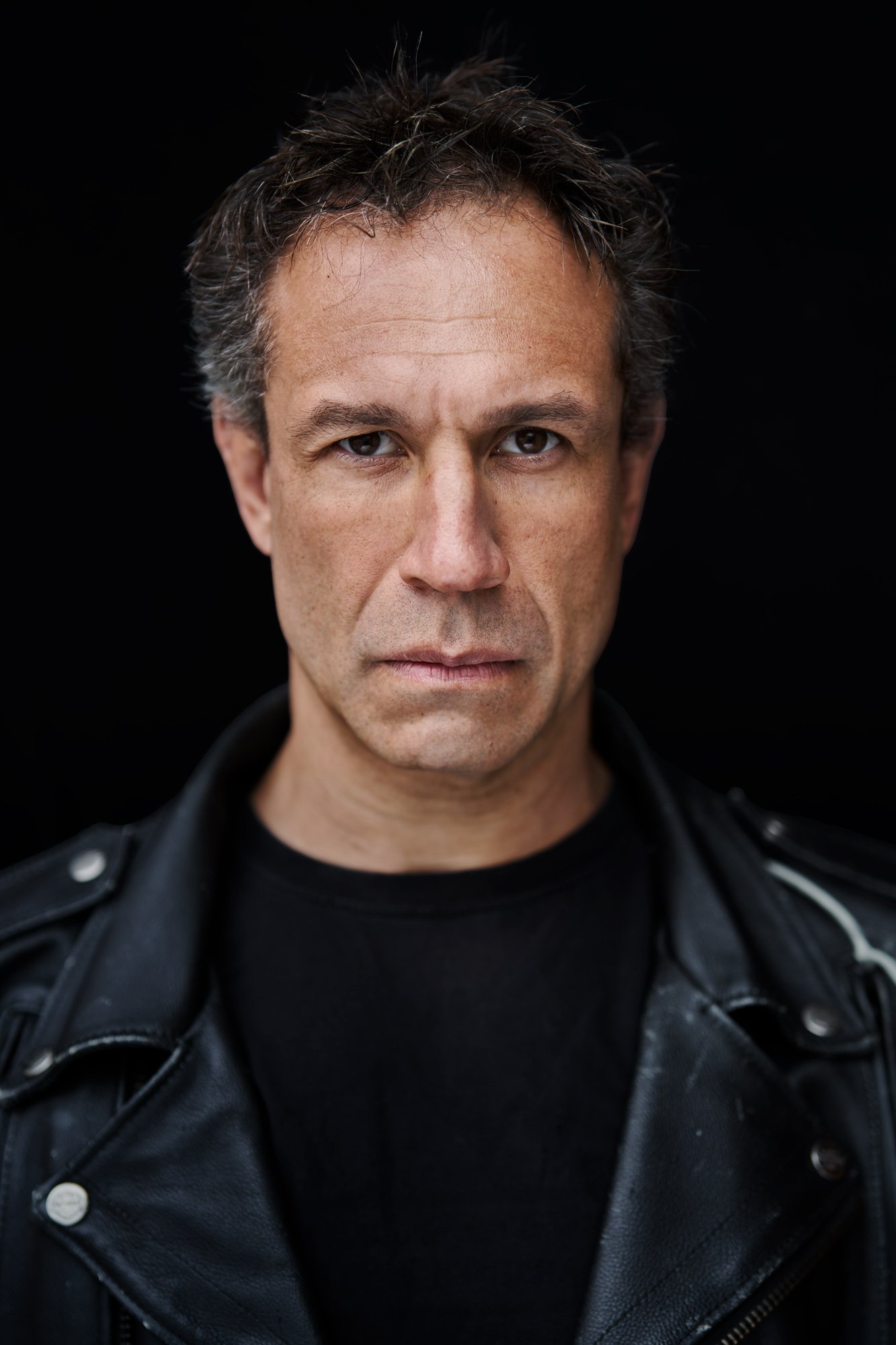 Headshot von Evil Jared Hasselhoff (Bloodhound Gang) in schwarzer Lederjacke und schwarzem Shirt vor schwarzem Hintergrund, intensiver, ernster Blick in die Kamera, fotografiert von Koszki Photography Berlin.