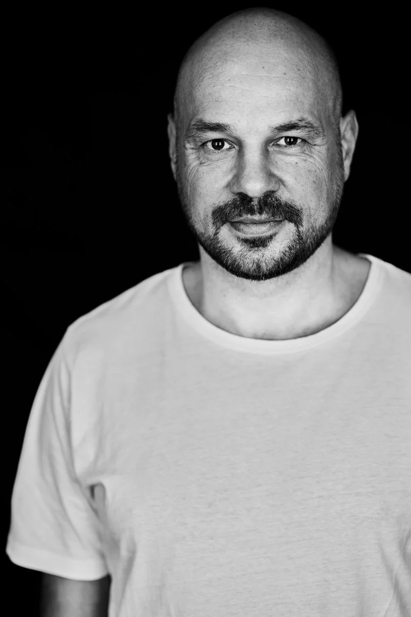 Schwarz-Weiß-Porträt des DJs D-Nox im weißen T-Shirt vor dunklem Hintergrund mit intensivem Blick, fotografiert von Koszki Photography Berlin.