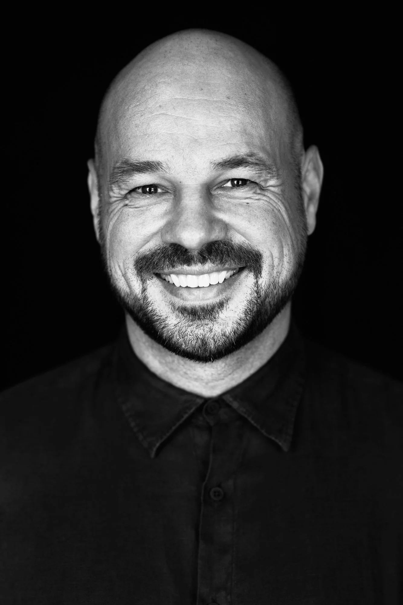 Schwarz-Weiß-Porträt des DJs und Produzenten D-Nox, herzlich lachend im dunklen Hemd vor schwarzem Hintergrund, fotografiert von Koszki Photography Berlin.
