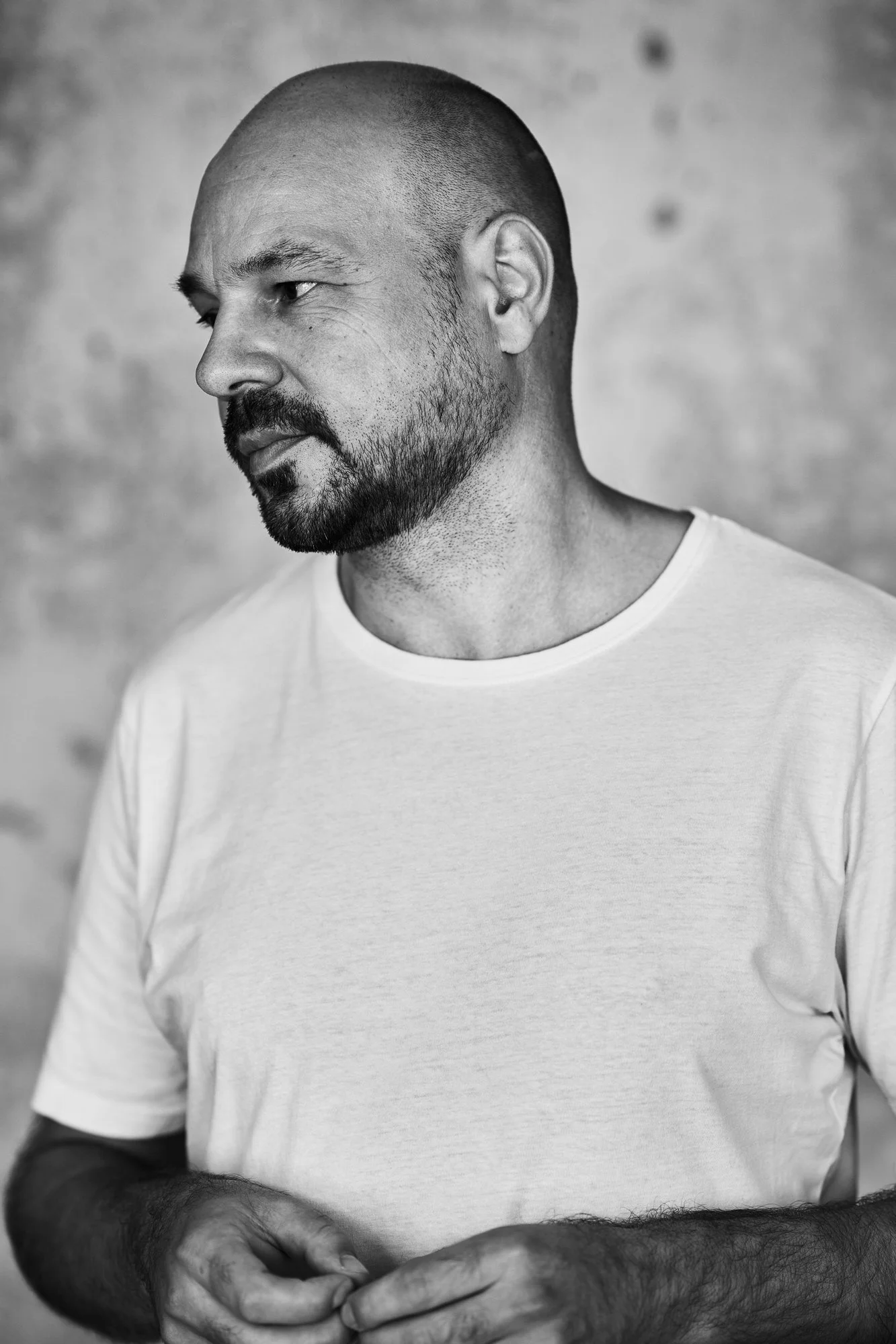 Schwarz-Weiß-Porträt des DJs und Produzenten D-Nox im weißen T-Shirt, den Blick seitlich gerichtet, vor einer strukturierten Wand, fotografiert von Koszki Photography Berlin.