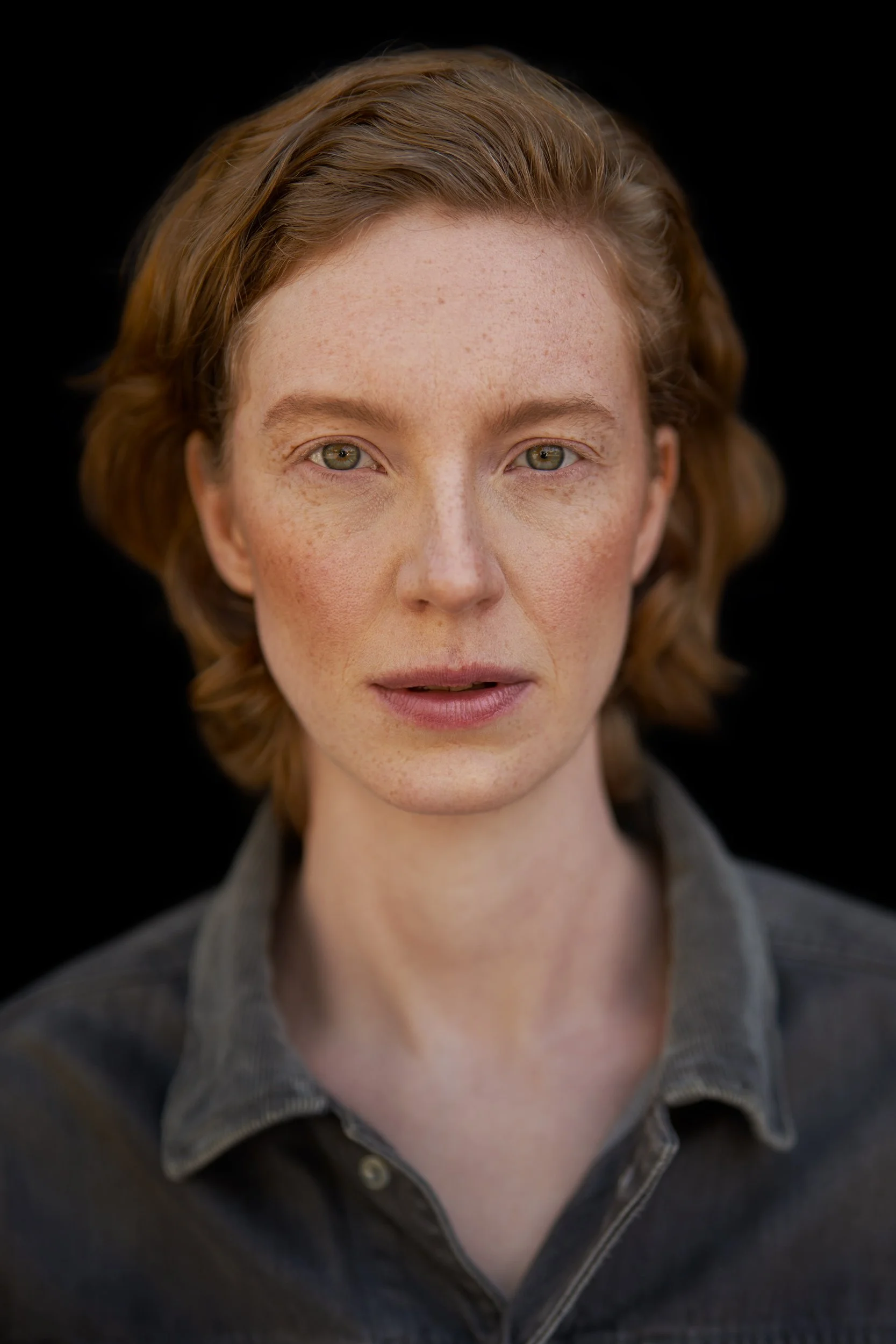 Headshot der Schauspielerin Luise Wolfram im dunklen Hemd vor schwarzem Hintergrund mit Sommersprossen und ruhigem Blick, fotografiert von Koszki Photography Berlin.