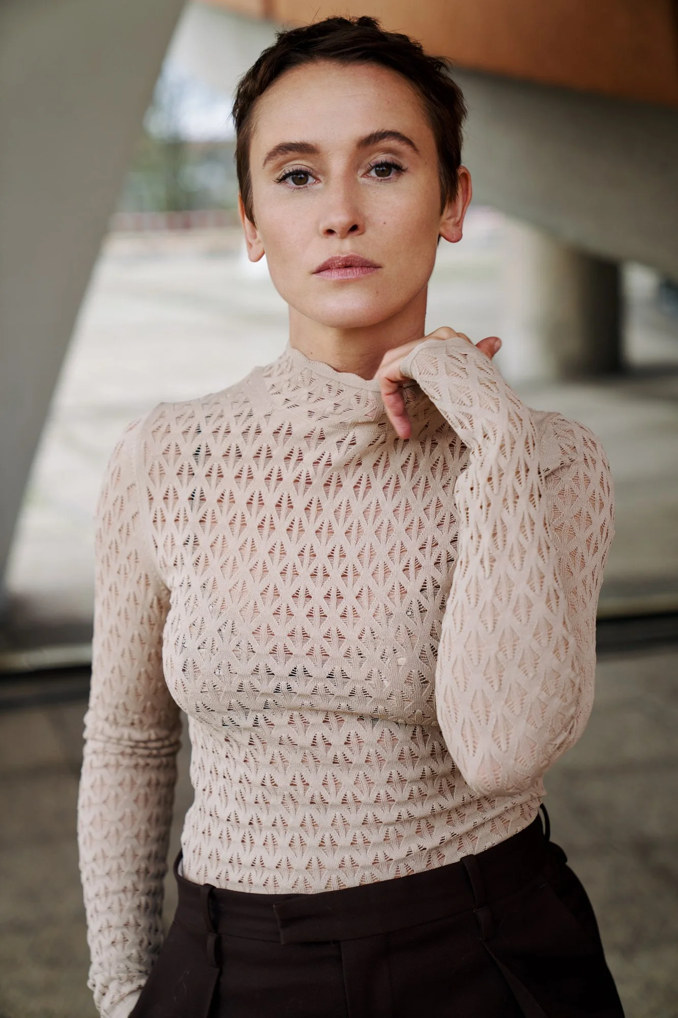 Porträtaufnahme der Schauspielerin Peri Baumeister in beigem Oberteil mit Lochmuster, die Hand am Kragen, direkter Blick in die Kamera, fotografiert von Koszki Photography Berlin.