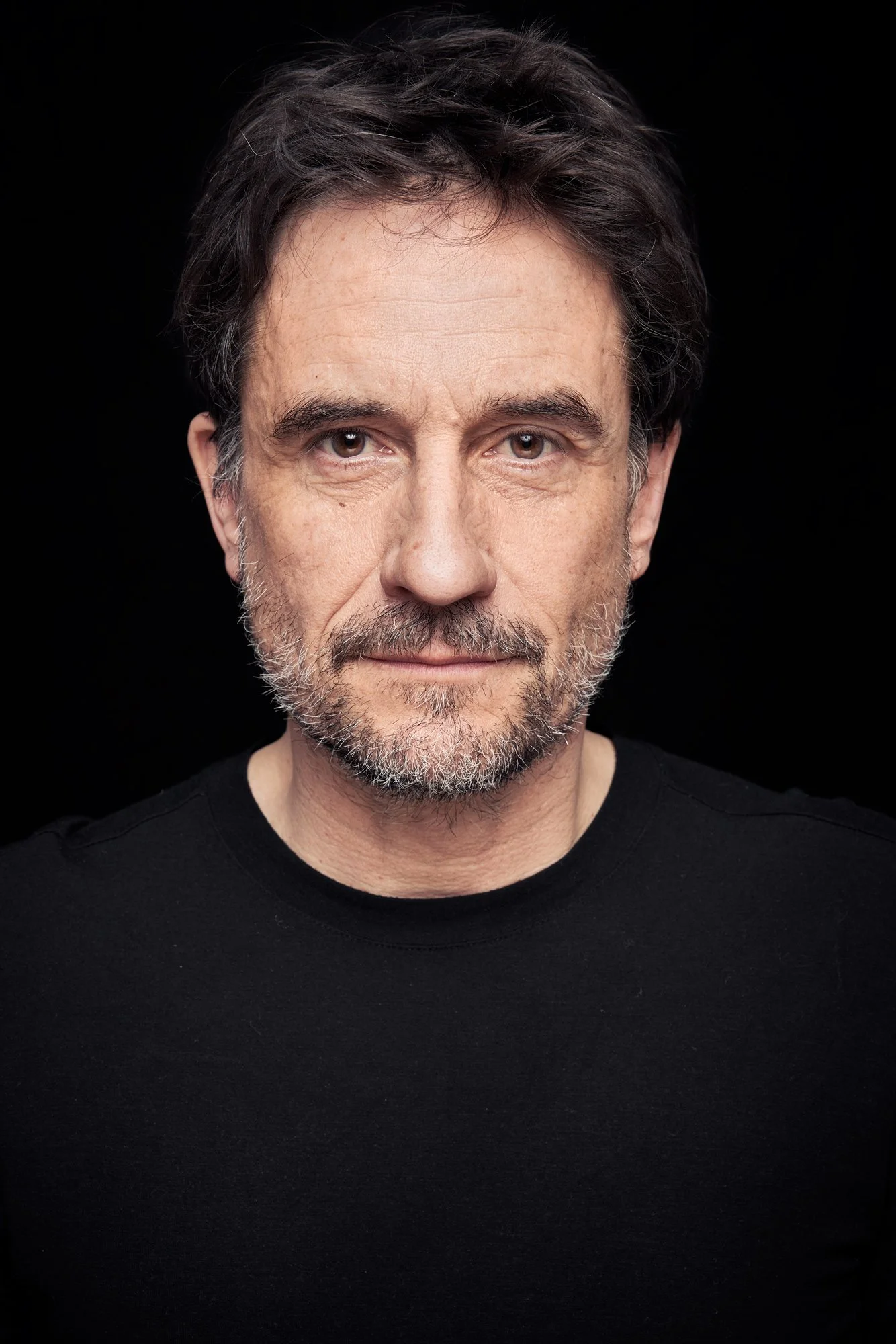 Headshot des Schauspielers Oliver Mommsen im schwarzen Shirt vor schwarzem Hintergrund, frontaler Blick in die Kamera, fotografiert von Koszki Photography Berlin.