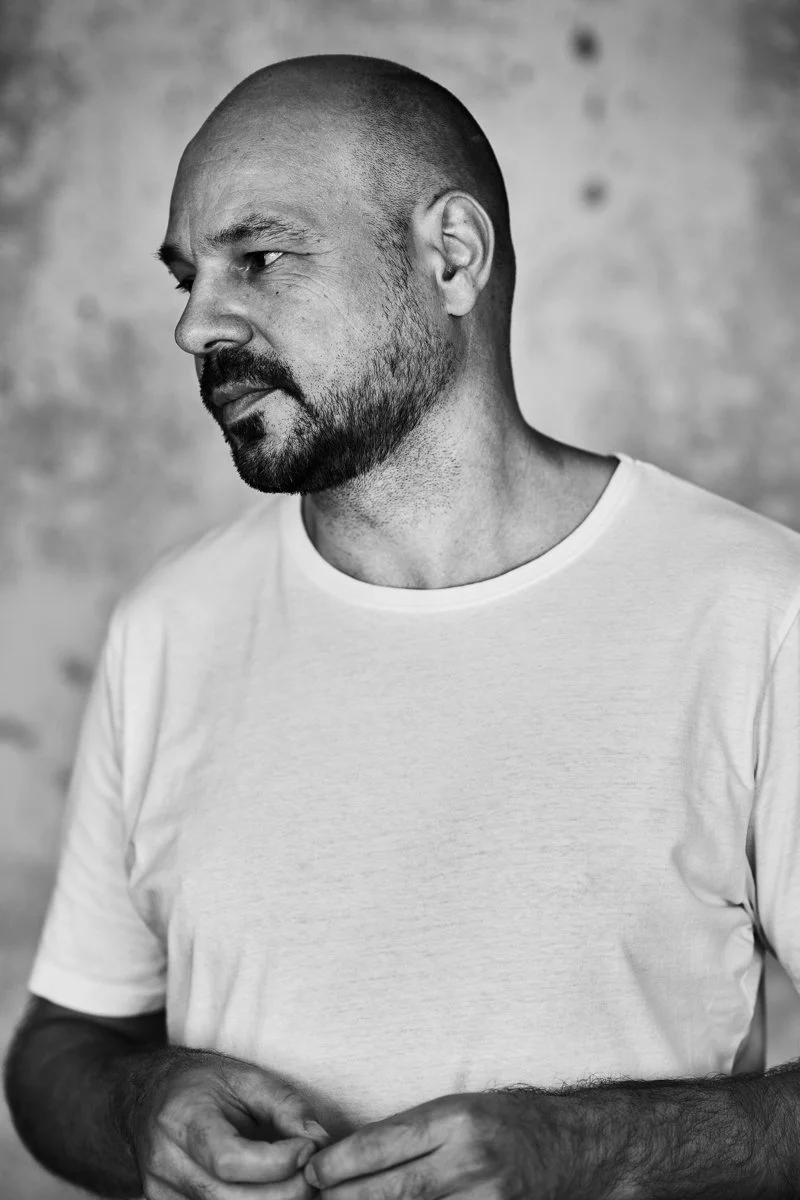 Schwarz-Weiß-Porträt des DJs D-Nox im weißen T-Shirt vor strukturierter Wand, den Blick seitlich gerichtet, fotografiert von Koszki Photography Berlin.