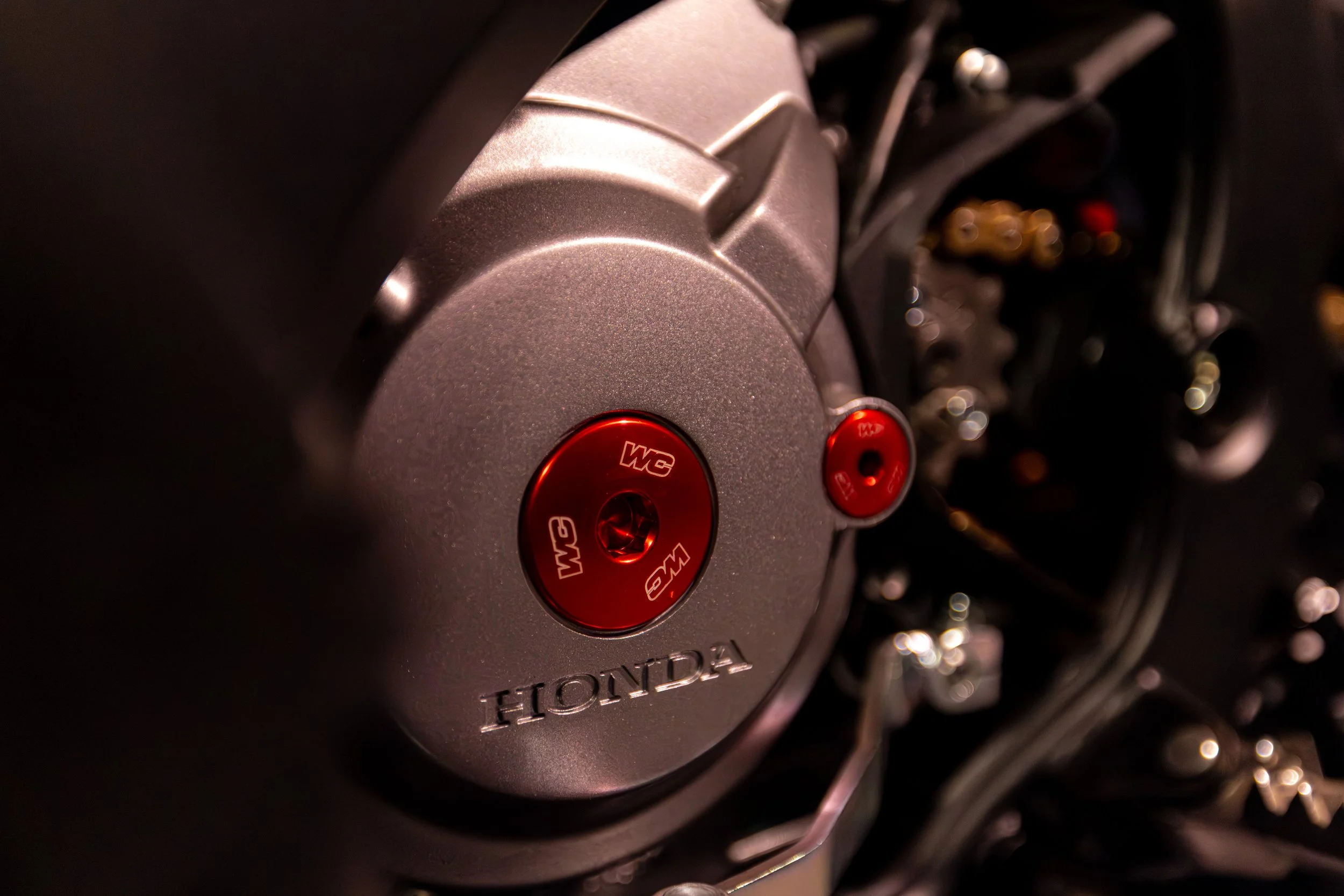 Close-up of a Honda motorcycle engine with a focus on the silver casing and red anodized bolts.