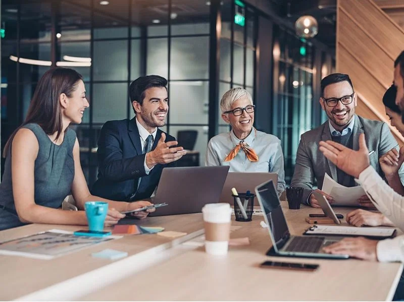Business team collaborating around a conference table with laptops and documents during an in‑office meeting.