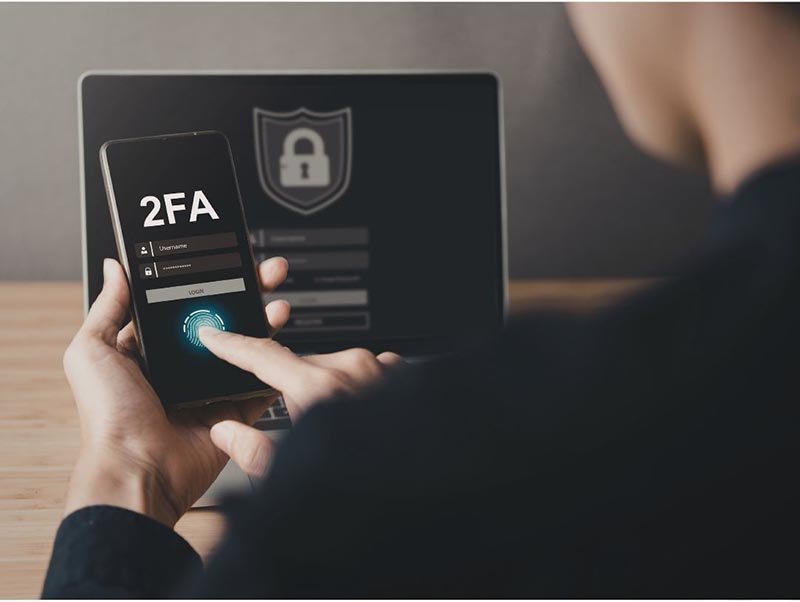 User authenticating with two-factor authentication on a smartphone using fingerprint scan, with a secure login screen visible on a laptop in the background.