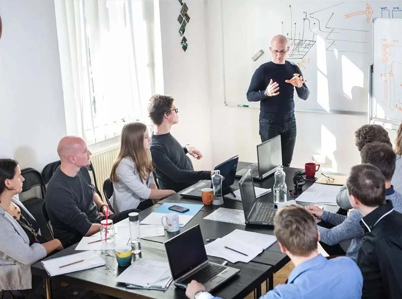 Technology team discussing cybersecurity and AI strategy during a collaborative office meeting with laptops and a whiteboard presentation.