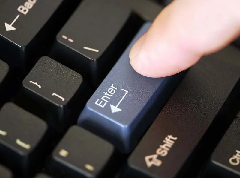 Close-up of a finger pressing the Enter key on a computer keyboard.