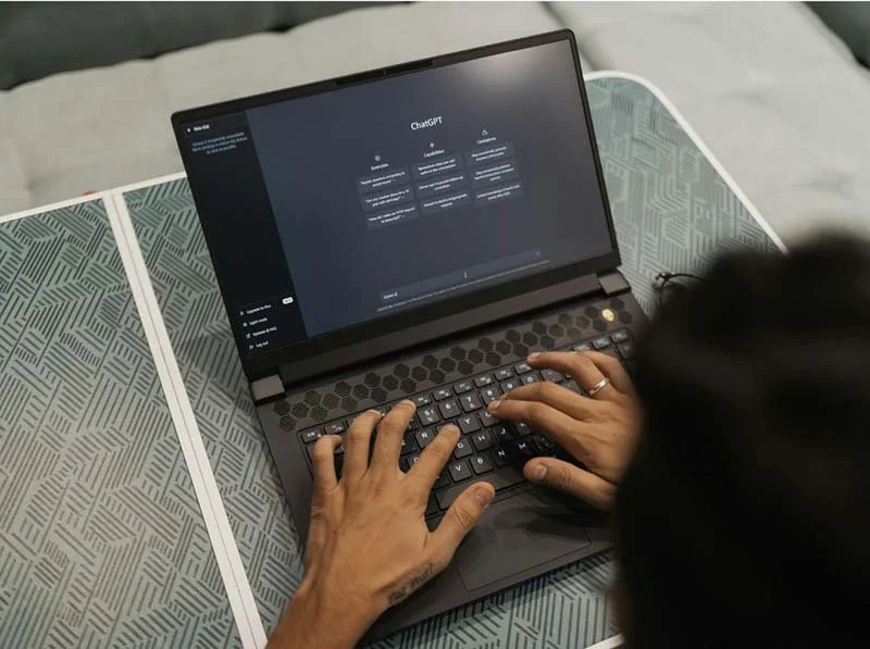 Overhead view of a person typing on a laptop displaying the ChatGPT interface on the screen.