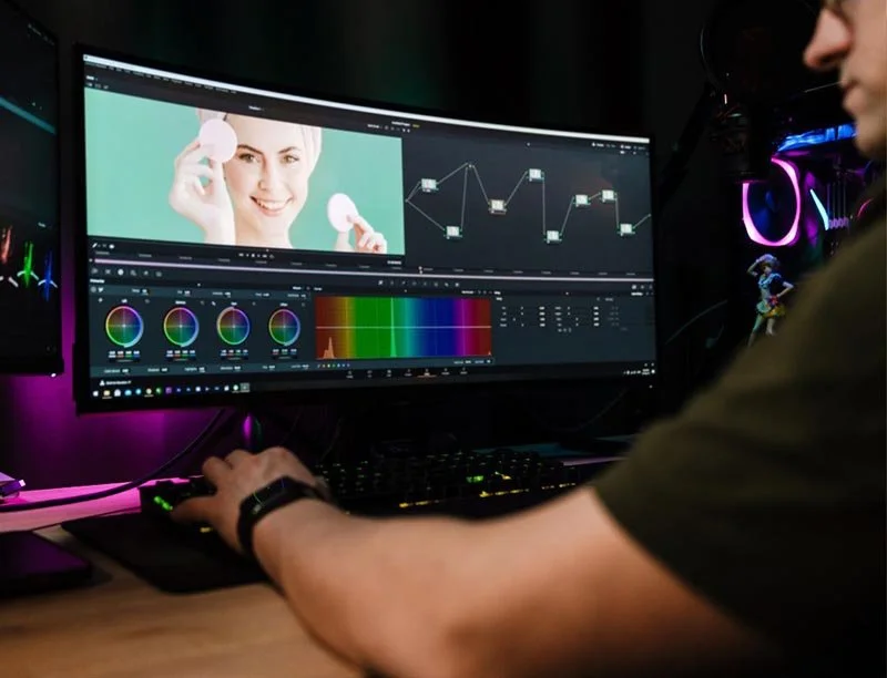 Person working on video color grading and editing software displayed on a wide monitor with color wheels and adjustment curves.