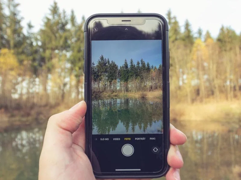 Smartphone held in hand capturing a photo of trees reflected in a calm forest pond