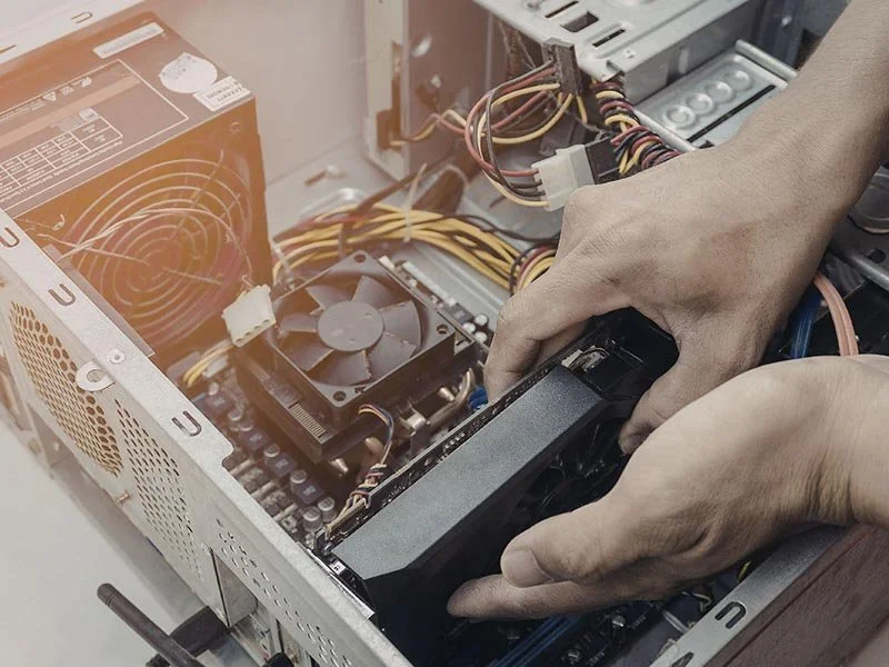 Hands installing a graphics card inside an open desktop computer case, with visible power supply, cables, and cooling fan.
