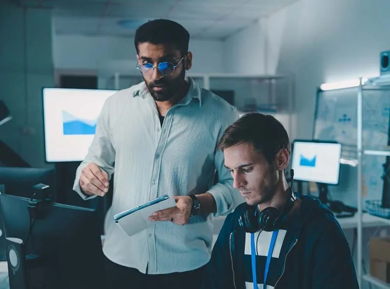 Technology professionals reviewing cybersecurity and AI-driven threat monitoring data at a computer workstation in a modern office.