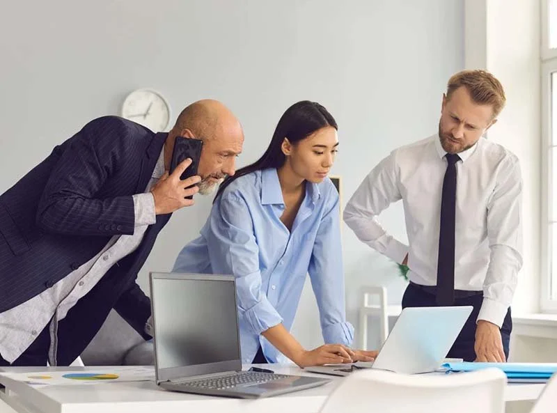 Three coworkers gathered around a laptop during a meeting in a bright office.