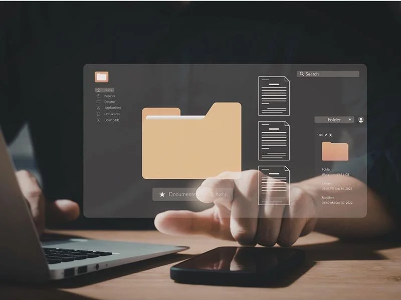 Hand interacting with a digital file management interface showing folders and documents on a laptop.