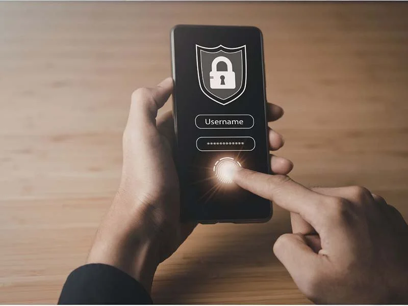 Hand holding a smartphone displaying a secure login screen with username, password field, and fingerprint authentication icon