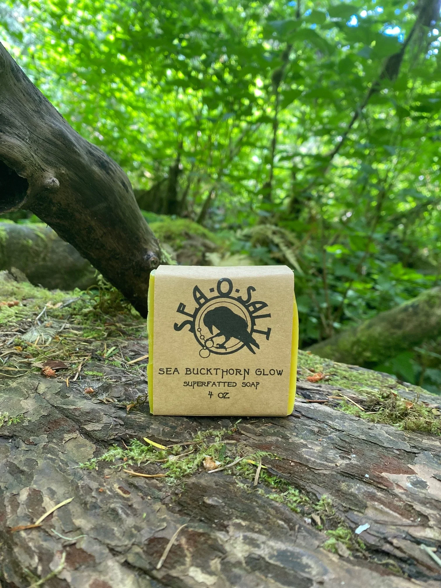 A bar of soap labeled 'Sea Buckthorn Glow' placed on a mossy log in a lush green forest with trees and leaves in the background.