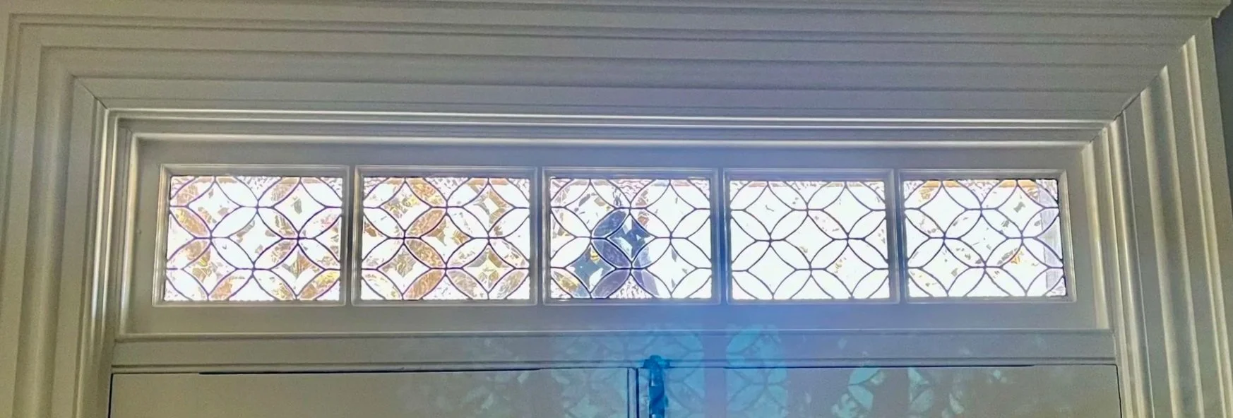 Decorative window panel with geometric patterns and stained glass accents above a door.