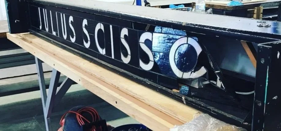 Close-up of a broken sign with partial letters and a globe symbol, resting on a wooden workbench in a workshop.