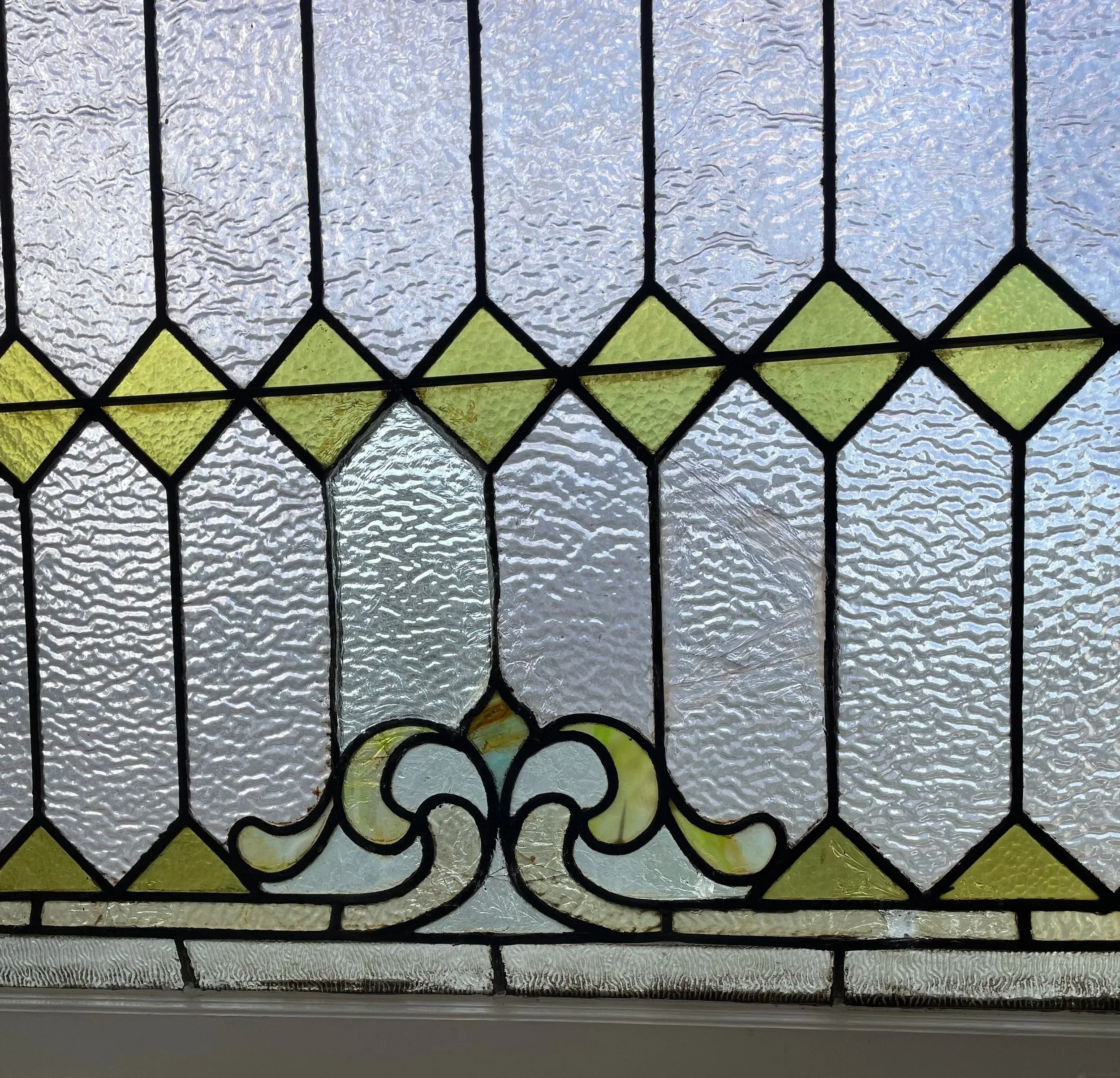 Decorative stained glass window with textured glass panes, green diamond-shaped accents, and an ornate vine-like design at the bottom.