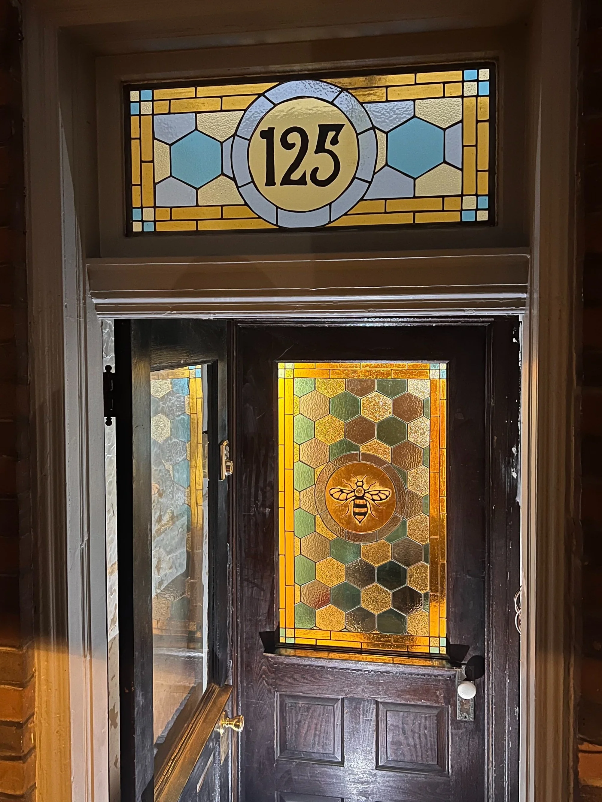 A decorative front door with stained glass featuring a bee and honeycomb pattern, with the house number 125 in a stained glass panel above the door.