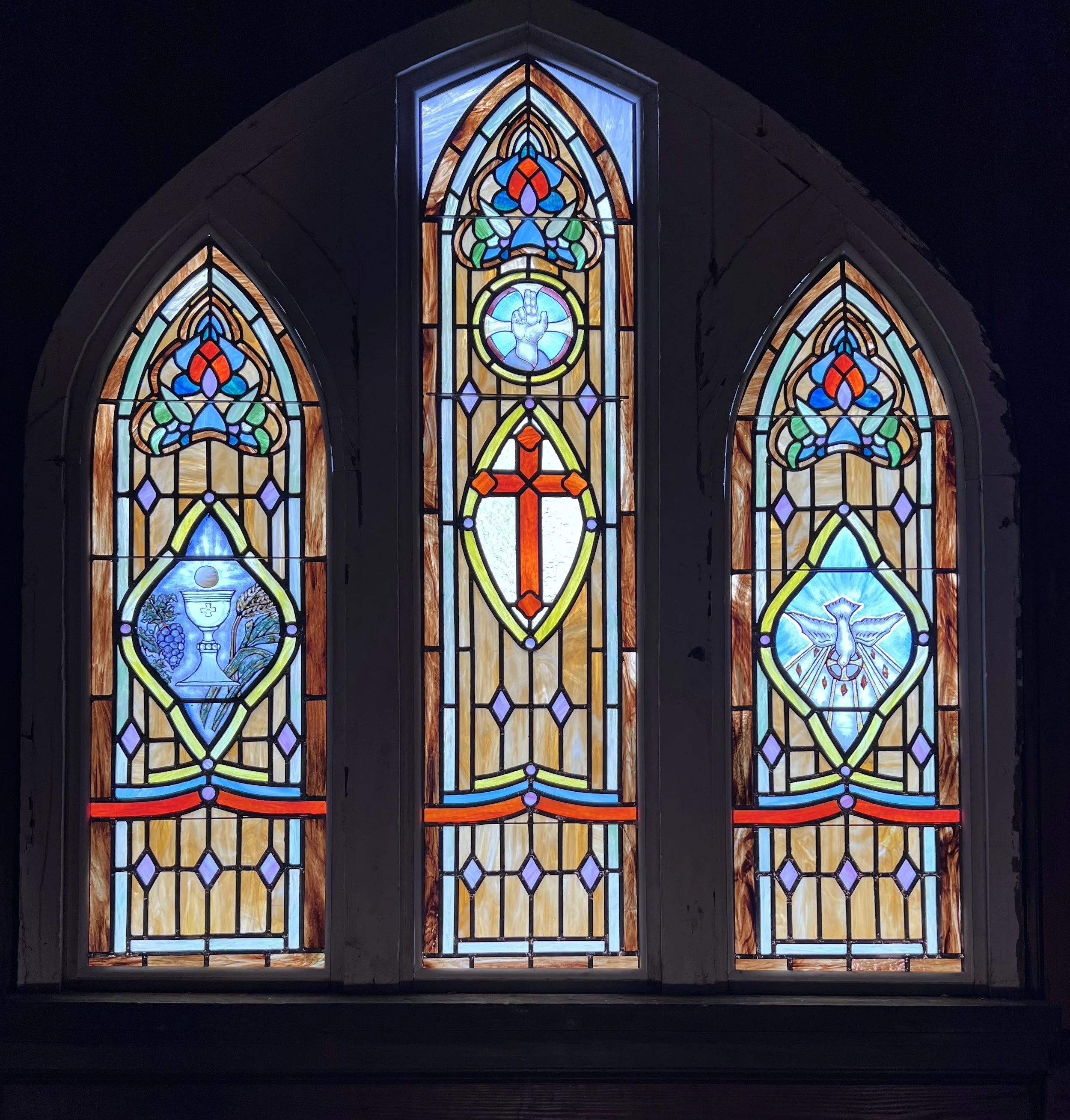 Colorful stained glass church windows featuring religious symbols including a cross, a dove, a chalice, and a crown.